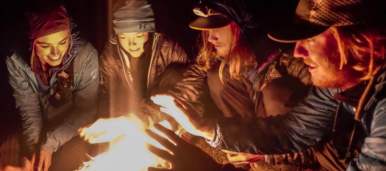 Students sit around a campfire. 