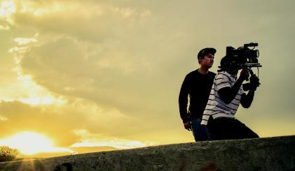 Two students taking video with a professional camera in the sunset