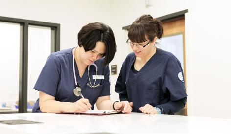 Two nurses reviewing paperwork on a clipboard