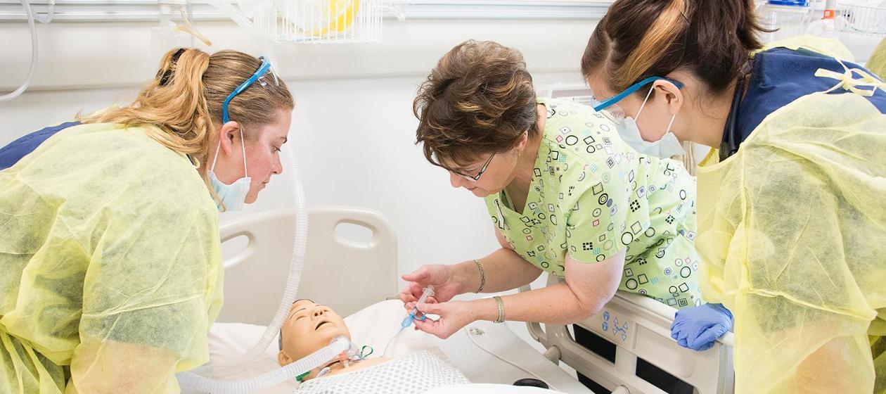 Two nursing students learn from a nursing professor in the simulation lab.