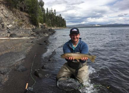 Will Polanksy is an outdoor ed alum. He is holding a fish he caught in a lake