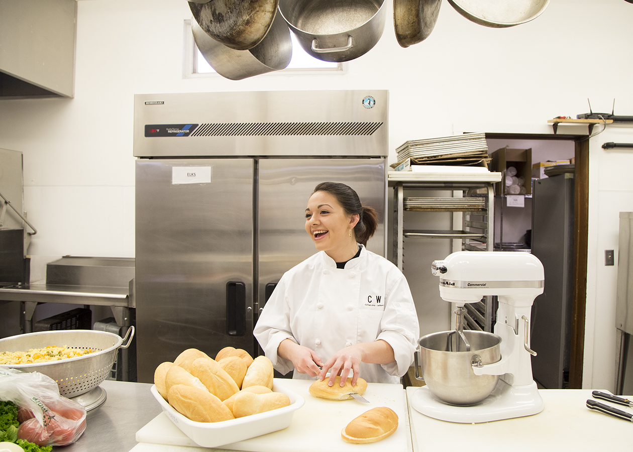 A female culinary student slices a loaf of bread in a kitchen