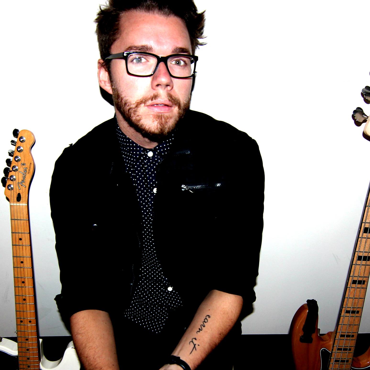 A cwc alumnus sits with two guitars on either side of him