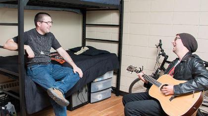 Two guys hanging out in a dorm room with a guitar